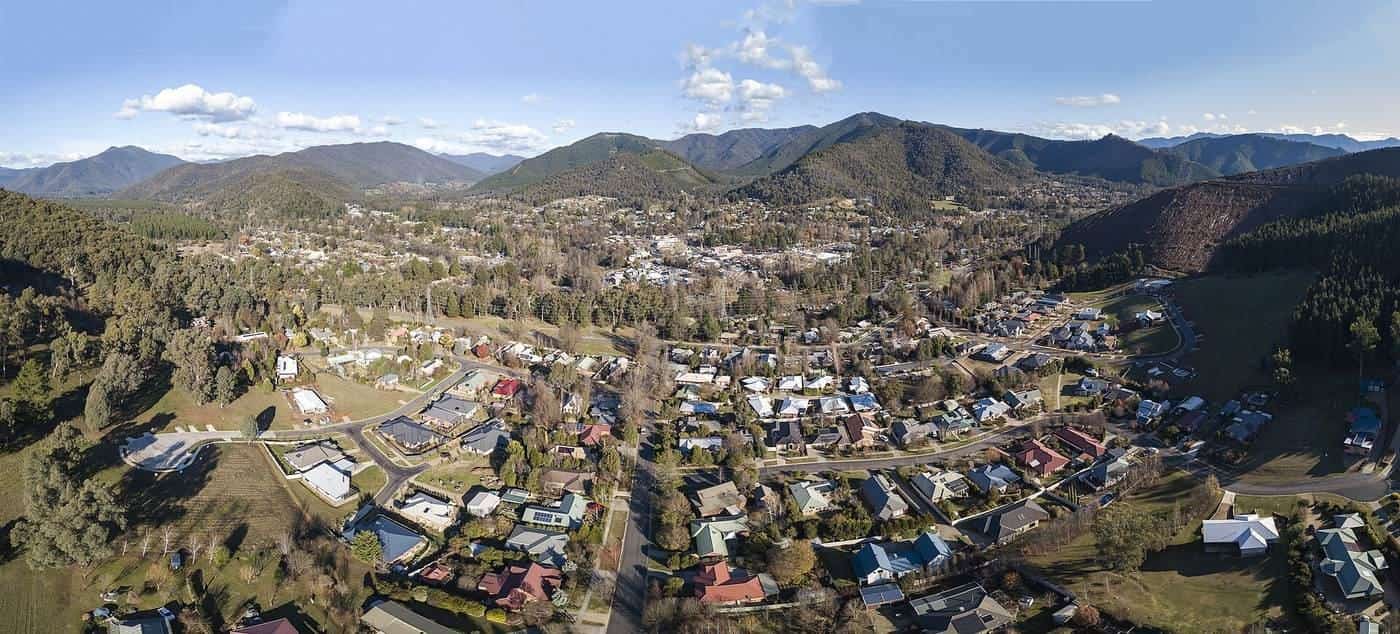 An aerial panorama of Bright, Victoria, nestled in a green valley surrounded by forested mountains