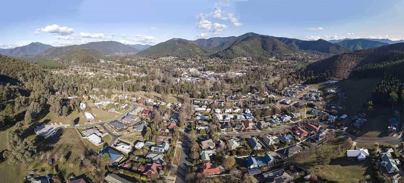 An aerial panorama of Bright, Victoria, nestled in a green valley surrounded by forested mountains